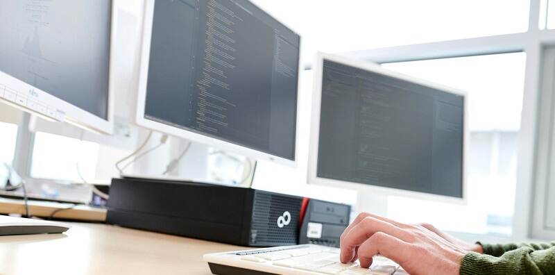 afbeelding van drie computerschermen en een toetsenbord